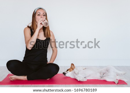 cute small jack russell dog sitting on a yoga mat at home with her owner drinking water. Healthy lifestyle indoors