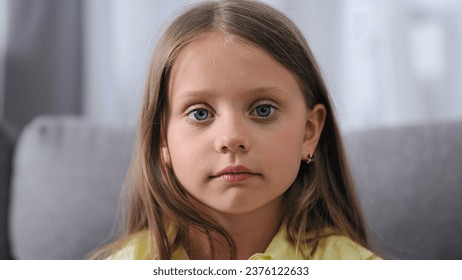Cute small kid look camera. One unhappy child sit sofa. Blue eyes gaze close up. Serious face portrait. Sad little girl cry. Brown hair model. Upset head shot. Young pretty person pose. Bad school day