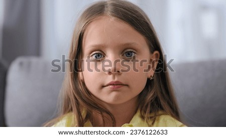Cute small kid look camera. One unhappy child sit sofa. Blue eyes gaze close up. Serious face portrait. Sad little girl cry. Brown hair model. Upset head shot. Young pretty person pose. Bad school day