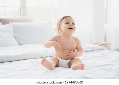 Cute small little newborn baby wearing a diaper sitting on white blanket in nursery bed. Child kid after bath shower. Infant daughter son nappy change and skin care. Childhood concept