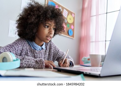 Cute smart african american school pupil kid girl virtual distance learning online watching remote digital class lesson looking at laptop computer tech studying at home writing notes sitting at desk.