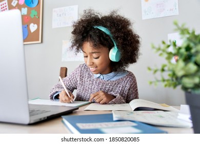 Cute smiling african school kid girl wearing headphones virtual distance learning online listening remote education digital class doing homework studying at home classroom sitting at desk with laptop.