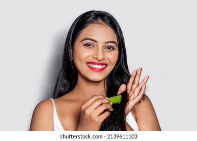 A Cute Smiling Asian Woman Applying Green Aloe-Vera Leaf Gel On Hair And Gives Hair Care Concept. Isolated On Gray Background.