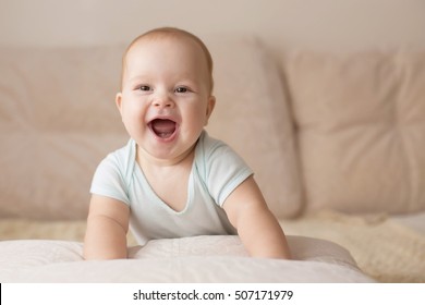 Cute Smiling Baby In A Blue Body Suit On A Beige Couch.