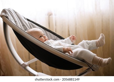 Cute smiling baby laying in bouncer chair. Child relaxing in a swing. Adorable newborn baby in bodysuit in sunny bedroom. Family morning at home.