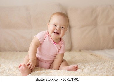 Cute Smiling Baby In Pink Bodysuit On A Beige Couch