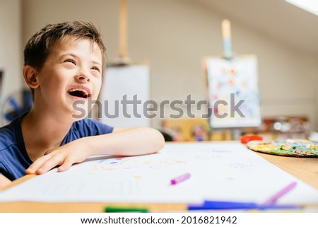 Cute smiling boy with down syndrome playing with paint at painting studio for special need children.