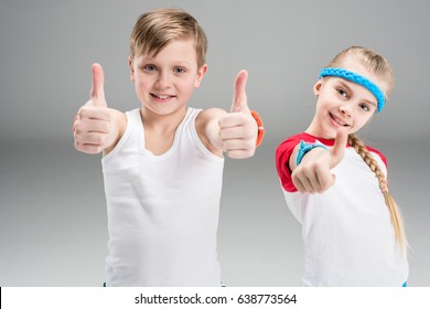 Cute Smiling Boy And Girl In Sportswear Showing Thumbs Up Isolated On Grey, Children Sport Concept