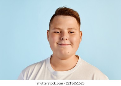 Cute smiling boy looking at camera  Teen boy in white tee expressing positive emotions isolated over blue background  Kids emotions concept  Closeup kid's face and fat cheeks