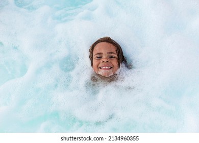 Cute smiling boy playing in the bubbles of a hot tub spa or bath tub. Fun, happy expression of a cute African American boy playing in the foamy water	