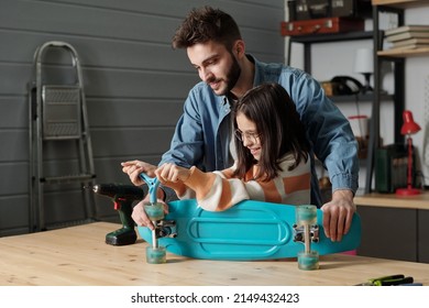 Cute smiling girl with handtool fixing wheels of skateboard on wooden table in garage while young man in denim shirt helping her - Powered by Shutterstock