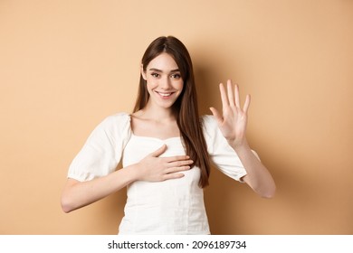 Cute Smiling Girl Make Promise, Put Hand On Heart And Tell Truth, Being Honest, Swearing To You, Standing On Beige Background