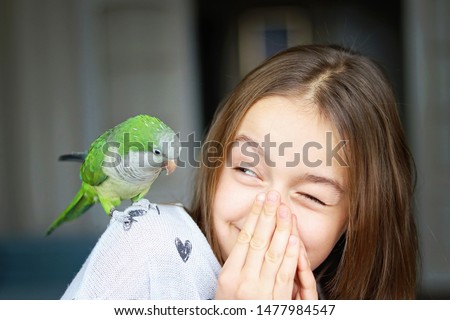 Cute smiling girl playing with her pet green Monk Parakeet parrot. who is sitting on her shoulder. Quaker parrot bird owner. Exotic pet. 