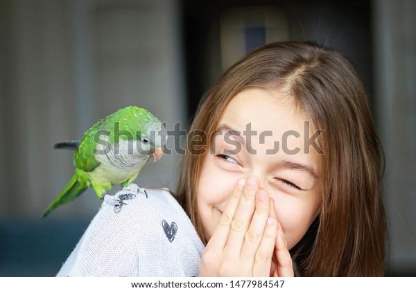 Cute smiling girl playing with her pet green Monk\
Parakeet parrot. who is sitting on her shoulder. Quaker parrot bird\
owner. Exotic pet. 