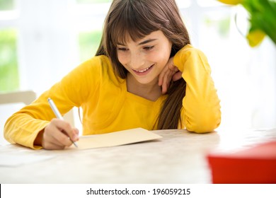 Cute Smiling Girl Writing A Letter Sitting At Desk 