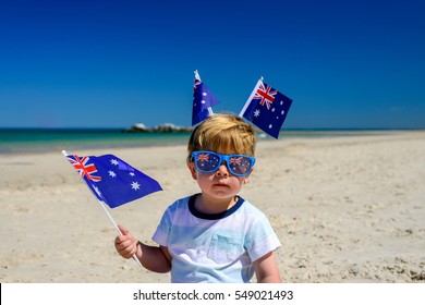 Cute smiling kid with Australian flags sitting on the sand at the beach on Australia Day - Powered by Shutterstock