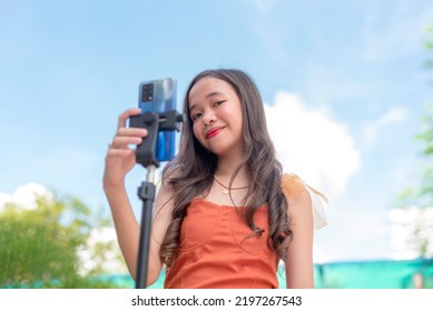 cute and smiling lady in her late teens sets up her phone mounted on a tripod as she prepares to make her video entry of the newest dance trend. - Shutterstock ID 2197267543