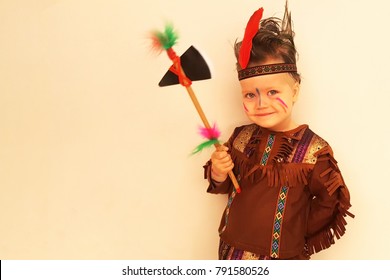 Cute Smiling Little Boy In An Indian Costume Posing Against The Wall, A Hatchet In His Hand, Hair Is Disheveled. Ready For Purim Party