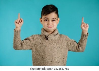 Cute Smiling Little Child Boy Pointing Up And Looking At The Camera On Blue Background. Human Emotions And Facial Expression