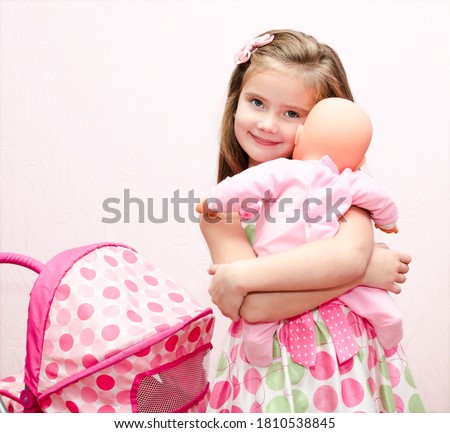 Cute smiling little girl child playing with her toy carriage and doll at home