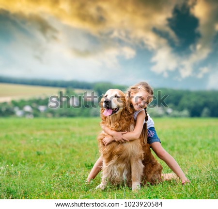 Cute smiling Little girl hugging retriever in the summer park