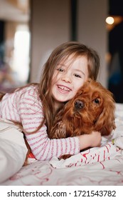 Cute Smiling Little Girl Hugs Dog On The Bed