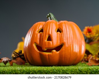 Cute Smiling Orange Pumpkin On Green Grass On A Gray Background. Halloween Symbol. Holiday, Food. There Are No People In The Photo. Advertising, Banner, Poster, Invitation.