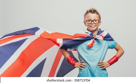 Cute smiling superhero boy posing with arms akimbo and wearing a British flag as a cape, learning languages concept