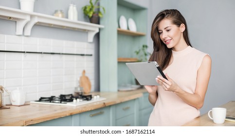 Cute smiling woman using digital tablet at home. Student girl reading or searching recipe. Online shopping, work from home, freelance, online learning, studying, self-care concept. Distance education - Powered by Shutterstock