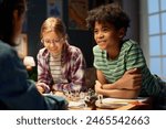 Cute smiling youthful boy in striped t-shirt looking at one of friends during discussion of rules or strategies of playing board game
