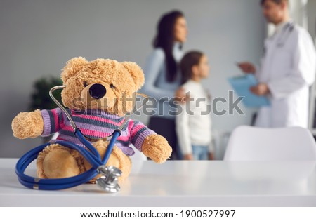 Cute soft teddy bear doctor with stethoscope sitting on table at pediatric clinic or children's medical center. Kids checkup visit to hospital, health maintenance concept. Blurred empty space for text