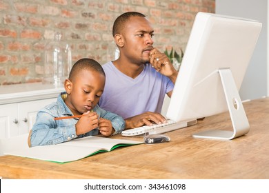 Cute son doing his homework with father in living room