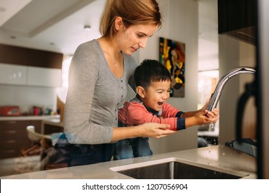 Cute Son Washing Hands With Support From His Mother In The Kitchen Sink. Woman Helping Little Boy To Wash Hands After Cooking.