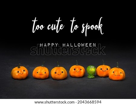 Too cute to spook. Happy Halloween. greeting card. cute orange pumpkin and green frog toy on black background. fall season. autumn time. symbol of halloween holiday.