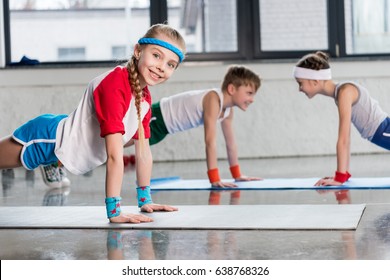 Cute sporty kids exercising on yoga mats in gym and smiling, children sport school concept