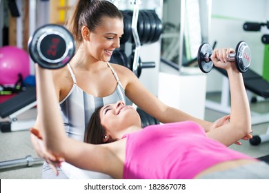 Cute Sporty young woman doing exercise in a fitness center with her personal coach. She is working exercises to strengthen her chest. - Powered by Shutterstock