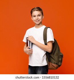 Cute Student. Teen Boy Ready For Getting Education, Smiling With Books And Backpack, Orange Background