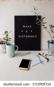 Cute styled workplace with inspirational text on black and white letter board, blank smartphone screen and notebook."Make a difference" goal setting words on personal desk. Work from home concept.