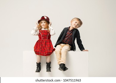 Cute stylish children on white studio background. Two beautiful teen girl and boy sittting together. Stylish young teen girl posing at studio. Classic style. Teen and kids fashion concept. children's