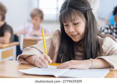 Cute successful learner of primary school, smiling asian School girl sitting in school writing in book with pencil, studying, education, learning. Asian children in the class. Student diversity.