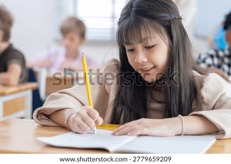 Cute successful learner of primary school, smiling asian School girl sitting in school writing in book with pencil, studying, education, learning. Asian children in the class. Student diversity.