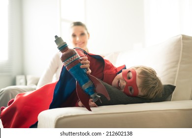 Cute superhero boy paying with toy rocket in the living room with his mother on background. - Powered by Shutterstock