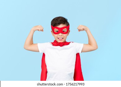 Cute superhero boy in red mask and cape flexing arm muscles isolated light blue background - Powered by Shutterstock