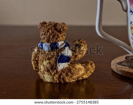 Cute Teddy Bear Back View Figurine With Textured Fur Wearing A Blue And White Scarf Sitting On A Dark Wooden Table As A Cozy Home Interior Decoration. Adorable Bear Sculpture Used As A Decorative Room Accent, Creating A Warm And Charming Atmosphere In A Stylish Living Space. Soft Furry Texture, Cute Animal Figurine And Cozy Interior Detail Perfect For Home Styling, Seasonal Winter Decor, Or Nursery And Bedroom Decoration