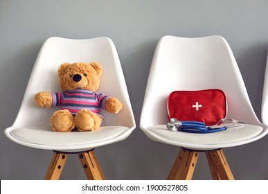 Cute Teddy Bear, First-aid Kit And Stethoscope On Two White Chairs In Children's Medical Center Or Pediatric Clinic Waiting Room. Kids' Visit To Hospital To See Pediatrician Or Family Doctor Concept