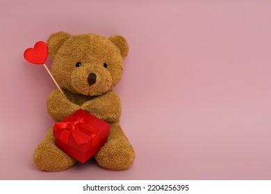 Cute teddy bear with red heart and gift box on pink background, space for text. Valentine's day celebration