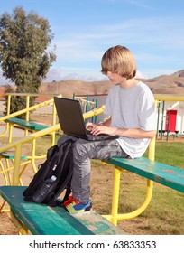 Cute teen aged boy sitting on bleachers working on his laptop.