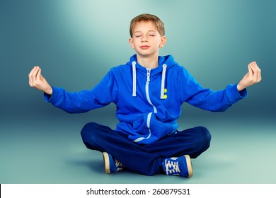 Cute teen boy sitting on the floor in a yoga pose and meditating. Studio shot.  - Powered by Shutterstock