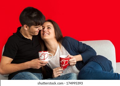 Cute Teen Couple Relaxing Together With Coffee On Couch.Isolated On Red Background. 