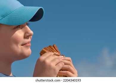 Cute Teen Girl Eating Cinnamon Bun, Side View. Child 11-13 Years Old Snacking On The Street, Face Close-up.